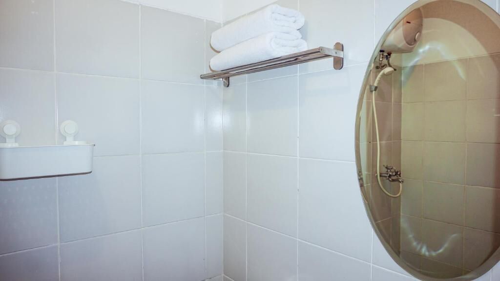A bathroom with white tiles, a glass-enclosed shower, a towel rack, and a small shelf with toiletries.