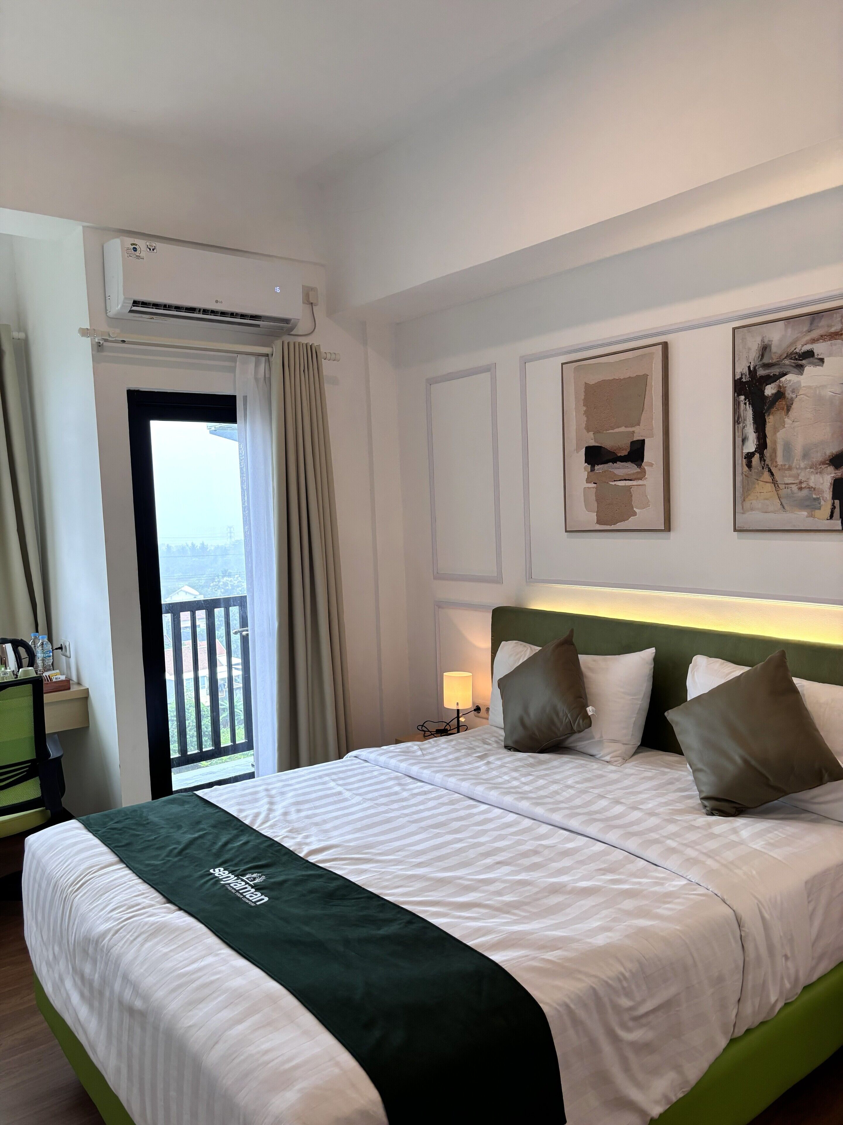 Een hotelkamer met een bed, een bureau, een stoel, uitzicht op een balkon en kunst aan de muur.