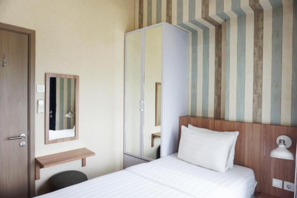 Habitación de hotel con una cama, un espejo, cabecera de madera, lámpara de noche y estante de madera.