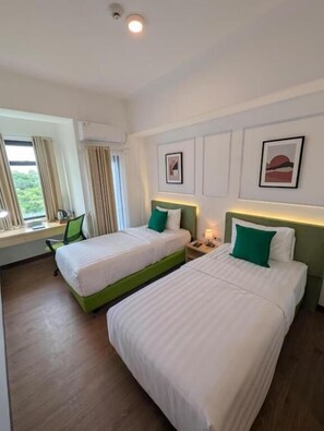Een hotelkamer met twee bedden, een bureau en een raam met gordijnen.