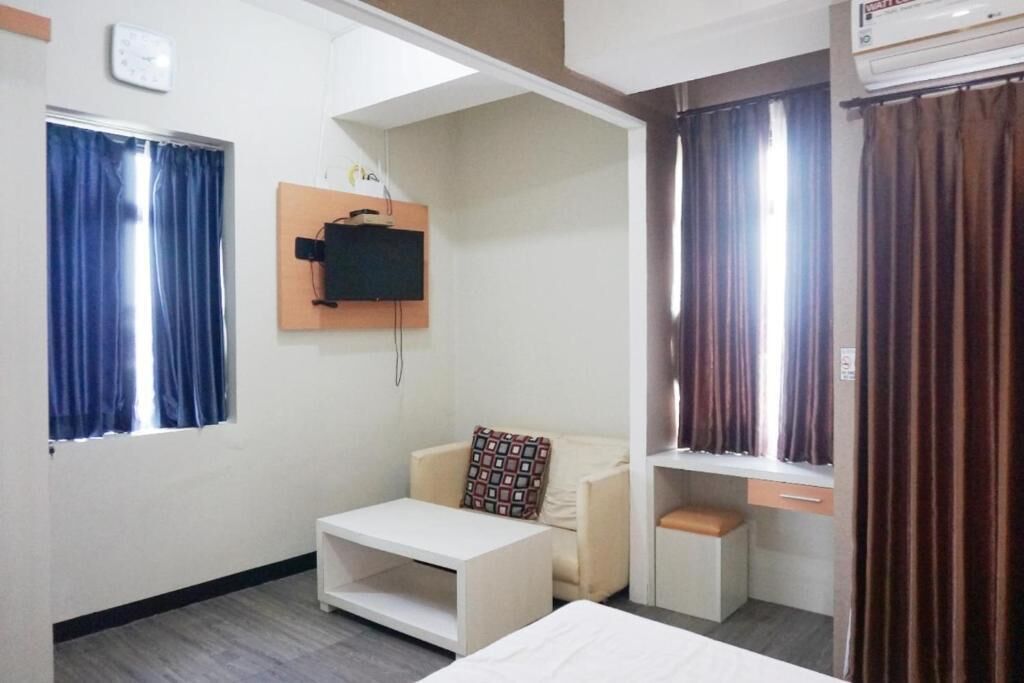 Una habitación con una cama, una pequeña mesa blanca, un sofá, un televisor montado en la pared y un ventanal con cortinas.