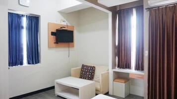 Una habitación con una cama, una pequeña mesa blanca, un sofá, un televisor montado en la pared y un ventanal con cortinas.