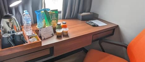 A hotel room desk with a lamp, water bottle, snacks, and a chair.