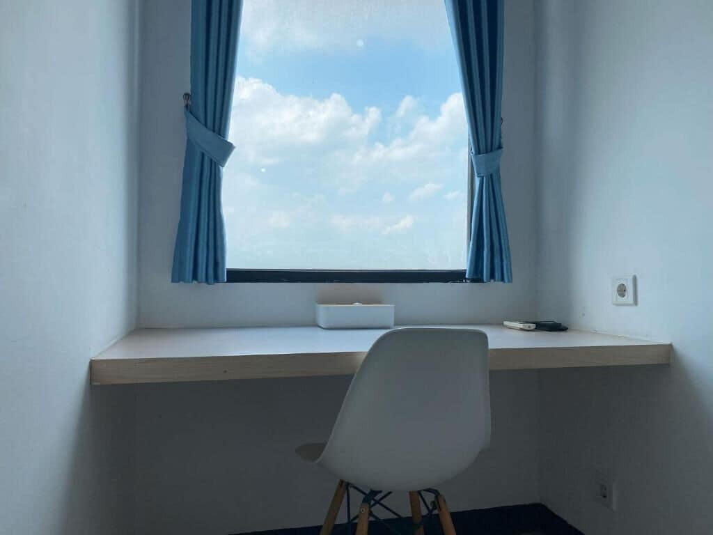 Een kamer met een bureau, een stoel, een raam met gordijnen en uitzicht op de lucht.