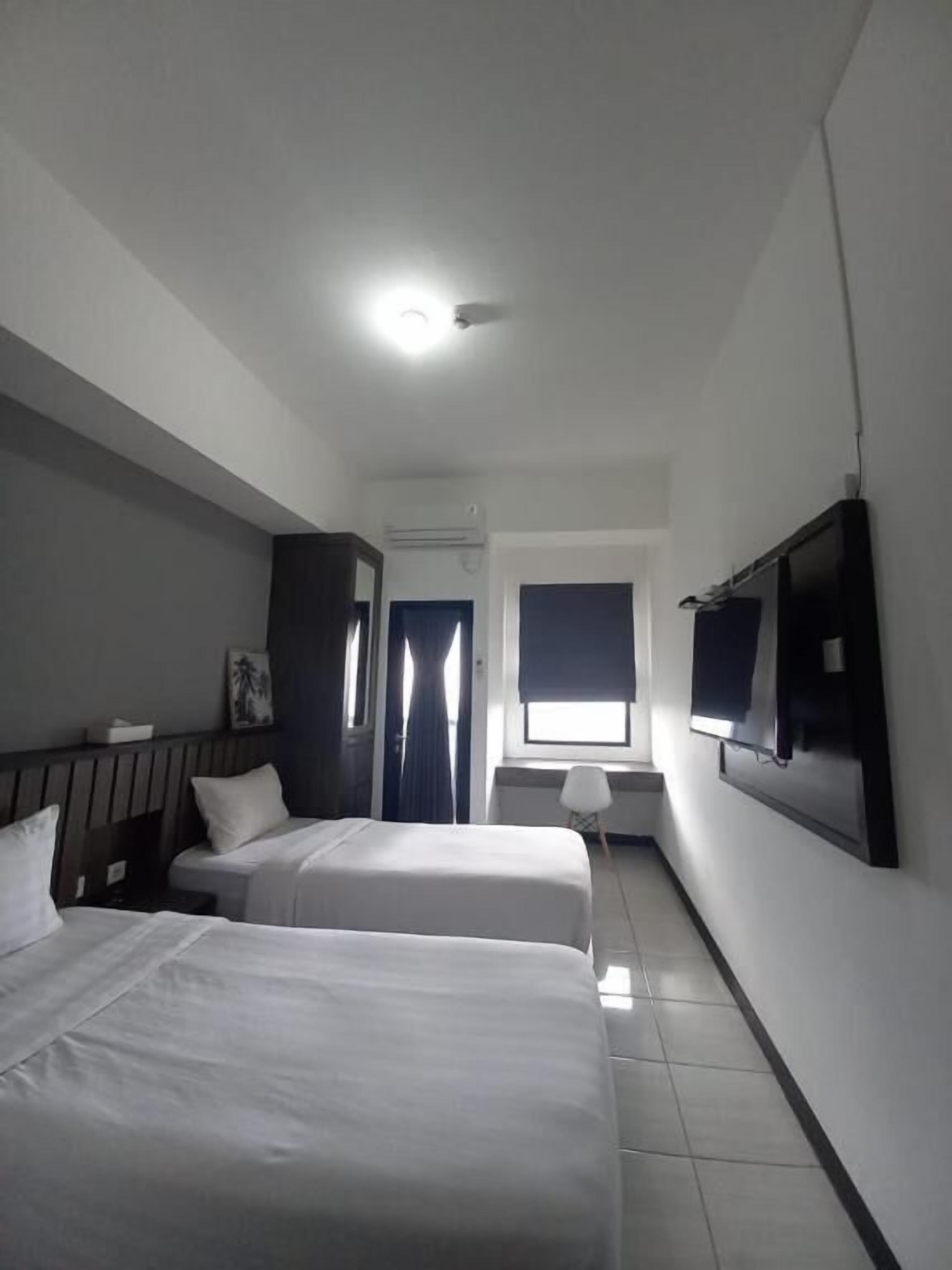 Een hotelkamer met twee bedden, een televisie, een raam met gordijnen en een plafondlamp.