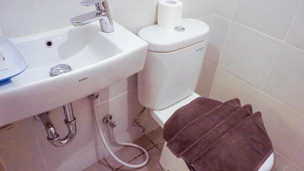 Casa de banho com lavatório branco, sanita e um porta-toalhas com toalhas.