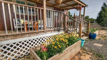 Une terrasse en bois avec une balustrade, un porche couvert et un parterre de fleurs jaunes.