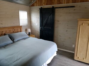 Et soveværelse med en seng, et natbord, en lampe, et træskab og en dør i lade-stil.