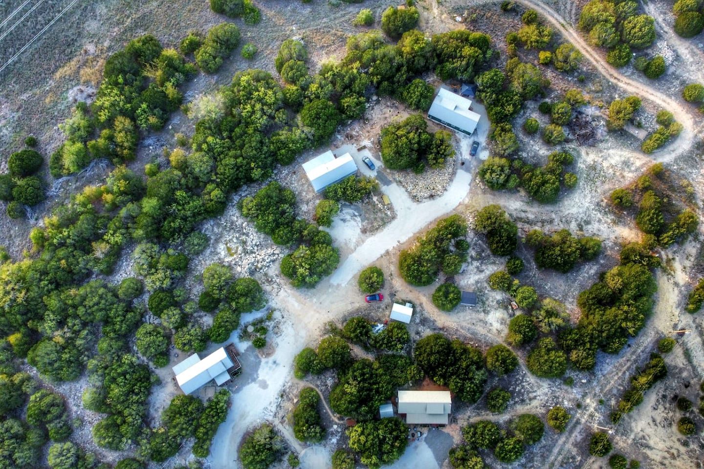 An aerial view of a property with multiple buildings, surrounded by dense greenery and a winding road.