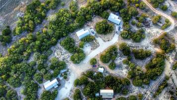 An aerial view of a property with multiple buildings, surrounded by dense greenery and a winding road.