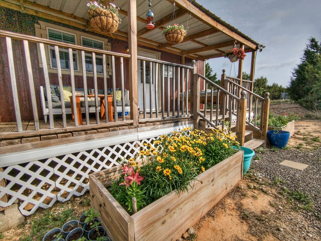 Eine Holzdiele mit Geländer, eine überdachte Veranda und ein Blumenbeet mit gelben Blüten.