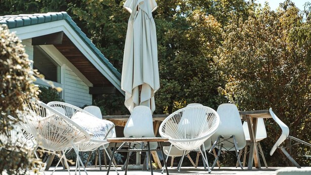 Outdoor seating with white chairs and a table, a white umbrella, and a building with a green roof in the background. - Tranquil Vacation Rental by Lake Wakatipu with Majestic Mountain Views in Queenstown, New Zealand (Queenstown)