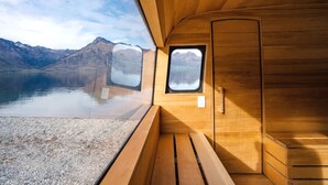 A cabin with a wooden interior, a window with a view of a lake and mountains, and a door. - Tranquil Vacation Rental by Lake Wakatipu with Majestic Mountain Views in Queenstown, New Zealand (Queenstown)