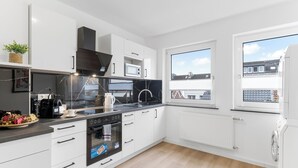 Une cuisine moderne avec des armoires blanches, un comptoir noir, un four encastré, un four à micro-ondes et un évier.