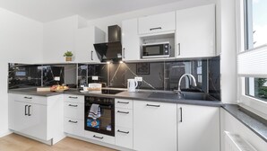 Une cuisine moderne avec des meubles blancs, un four à micro-ondes encastré, une cuisinière et une fenêtre laissant entrer la lumière naturelle.