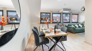 Un espace de vie moderne comprenant un coin repas, un canapé vert et une vue sur le paysage urbain grâce à de grandes fenêtres.