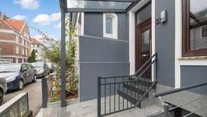 Un immeuble résidentiel à la façade grise, doté d’une porte en bois et d’une petite fenêtre.
