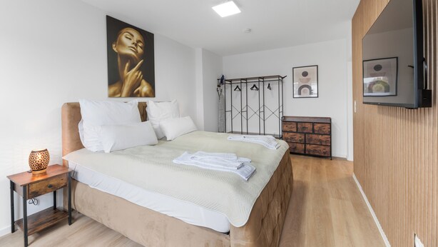 Une chambre à coucher comprenant un lit, une table de chevet, un téléviseur fixé au mur et une armoire.