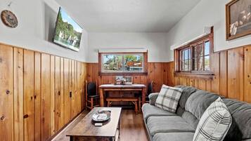 A cozy room with wooden walls, a wooden dining table, a sofa, and a TV mounted on the wall.