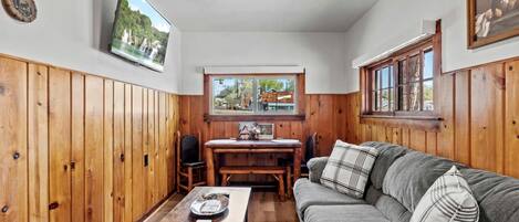 Une pièce chaleureuse avec des murs en bois, une table à manger en bois, un canapé et un téléviseur fixé au mur.