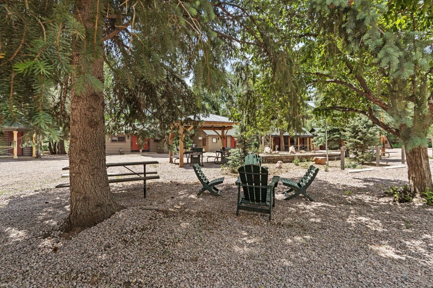 A rustic outdoor seating area with Adirondack chairs, a picnic table, and a wooden cabin in the background.