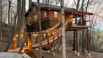 A wooden cabin with a deck and stairs, surrounded by trees.