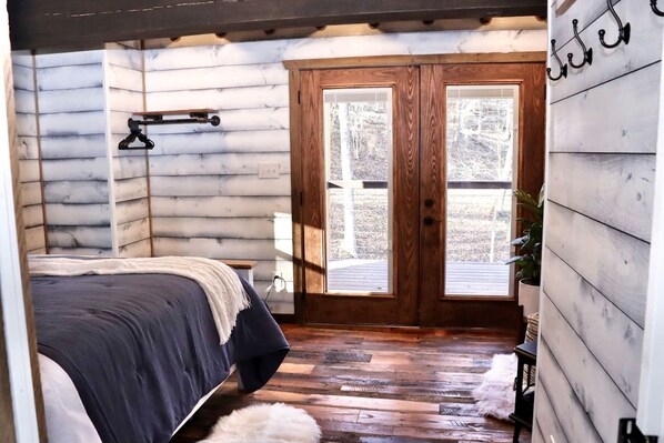 A log cabin bedroom with a bed, wooden floor, a wooden door, and a window.