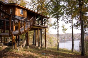 Una baita in legno con una veranda che si estende su una zona boschiva, con vista su un lago.