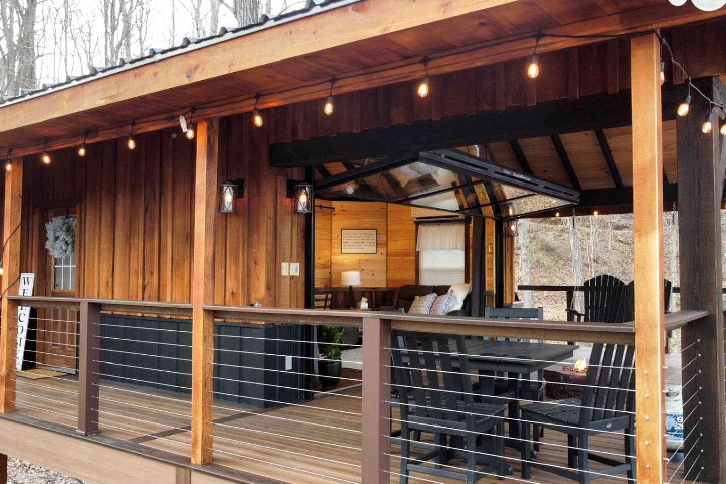 A wooden cabin with a covered deck, outdoor seating, and string lights.