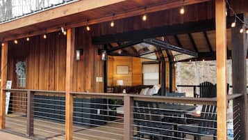 A wooden cabin with a covered deck, outdoor seating, and string lights.