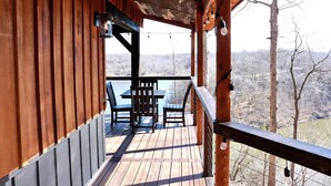 Eine Holzterrasse mit Tisch und Stühlen, die auf ein Gewässer und Bäume blickt.