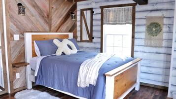 A wooden cabin-style bedroom with a bed, pillows, a blanket, and a wall-mounted lantern.