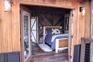 A wooden cabin bedroom with a bed, a window, and a door.