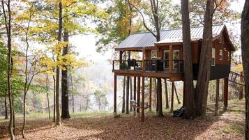 A treehouse with a balcony, surrounded by autumn foliage.