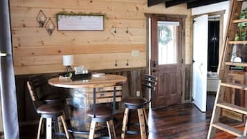A rustic wooden interior with a round table, four chairs, and a wooden barrel.