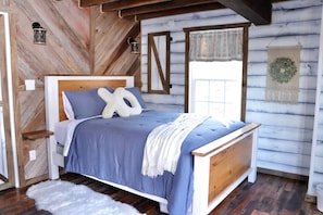 Ein schlicht eingerichtetes Schlafzimmer im Holzblockhaus-Stil mit einem Bett, Kissen, einer Decke und einer Wandleuchte.