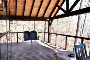 A wooden deck with a bench and a table, surrounded by trees.