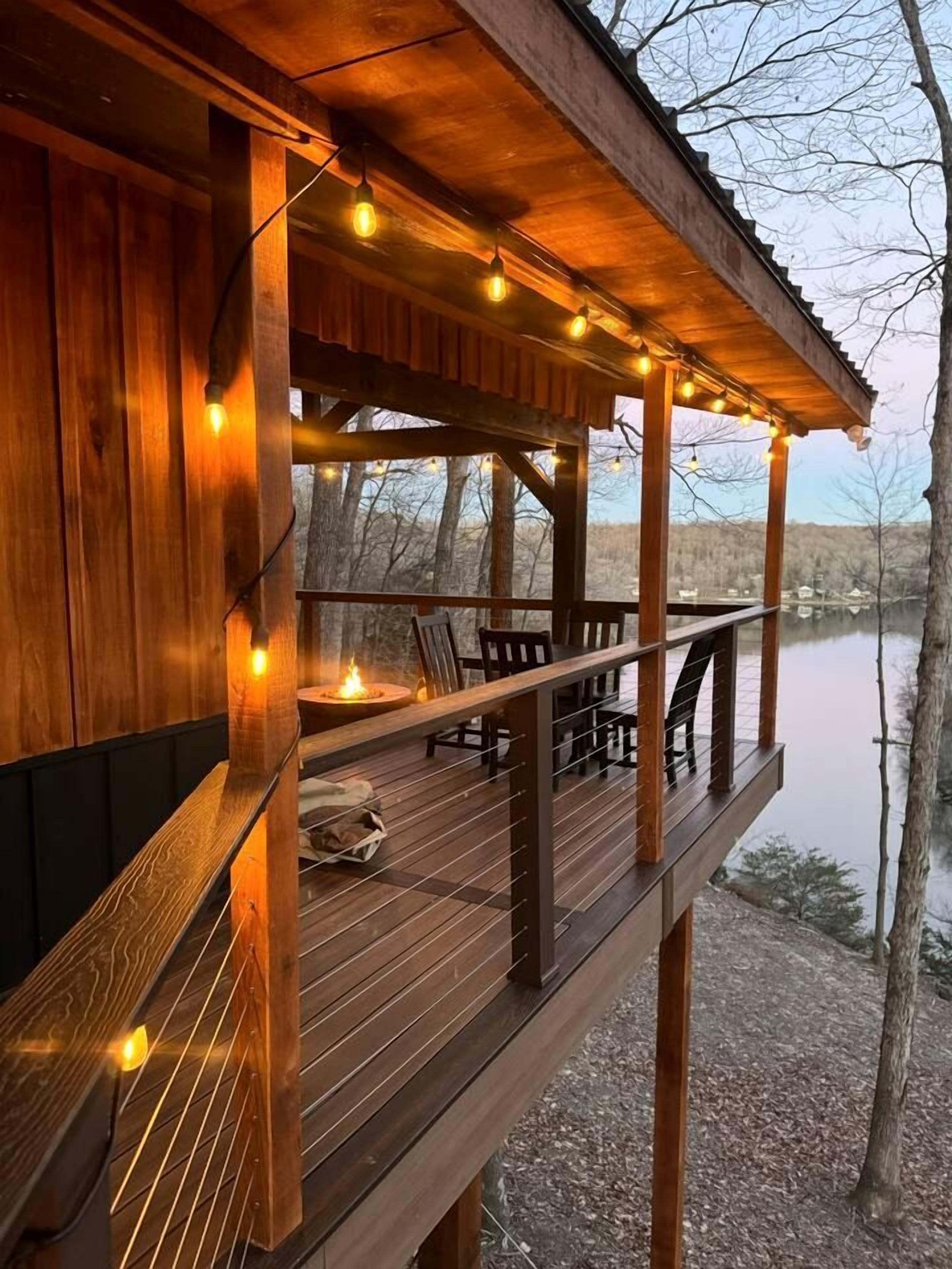 A wooden deck with string lights, a fire pit, and a view of a lake.