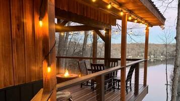 A wooden deck with string lights, a fire pit, and a view of a lake.