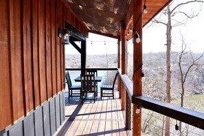 Um deck de madeira com mesa e cadeiras, com vista para um corpo de água e árvores.