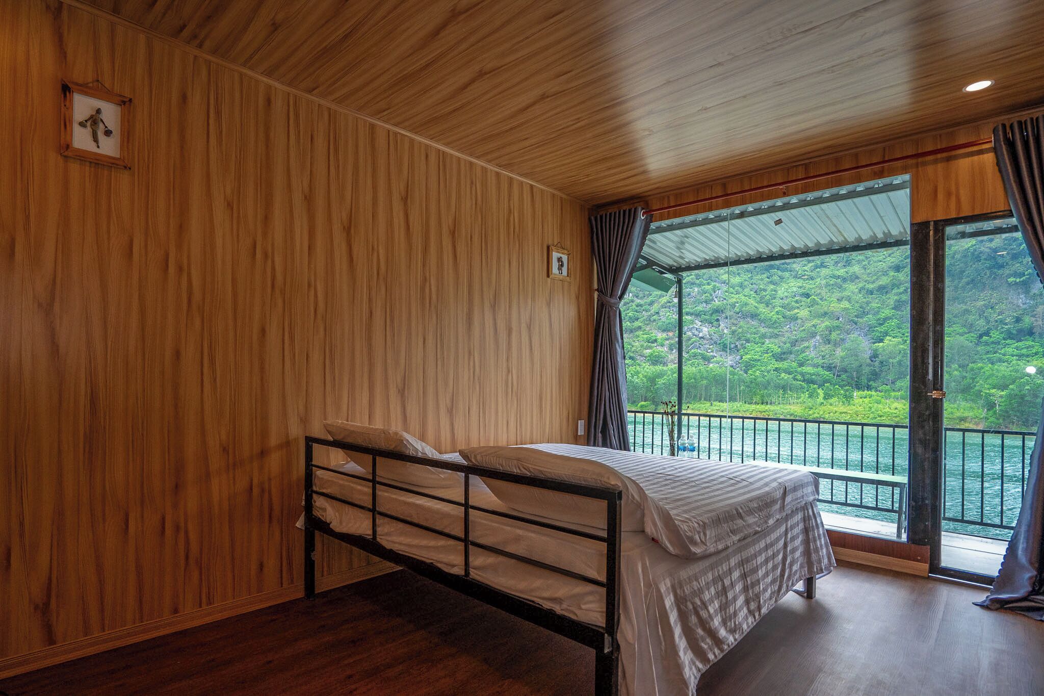 Ein Zimmer mit einem Bett, Holzwänden und einem großen Fenster mit Blick auf Grünflächen.