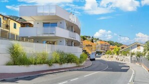 Un edificio moderno de varios pisos con balcones, una carretera curva y un cielo despejado.