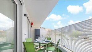 Un balcón con una mesa para dos, una puerta y una ventana con persianas.
