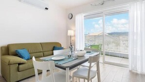 Una sala de estar moderna con sofá, mesa de comedor, sillas, una lámpara y vistas a través de puertas correderas de cristal.