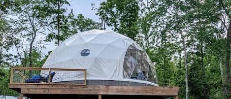 A geodesic dome structure with a wooden deck, seating area, and a small table.