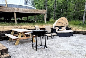Ett takförsett utomhusområde med bord och stolar, ett picknickbord och en rund sittgrupp under ett tak.