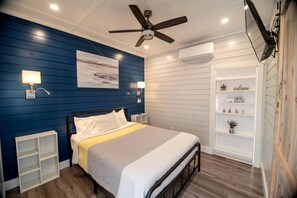 A bedroom with a bed, bedside tables, a ceiling fan, an air conditioning unit, and a built-in shelf with decorative items.