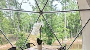 Un comedor con una mesa, sillas y vistas a un bosque a través de un ventanal amplio.