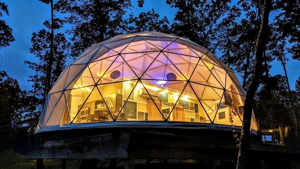 Una estructura en forma de domo geodésico con un interior visible, que incluye una zona de cocina y espacio para sentarse.