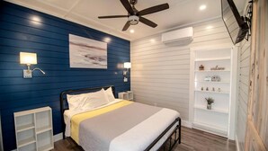 Un dormitorio con cama, mesitas de noche, ventilador de techo, equipo de aire acondicionado y estante empotrado con objetos decorativos.